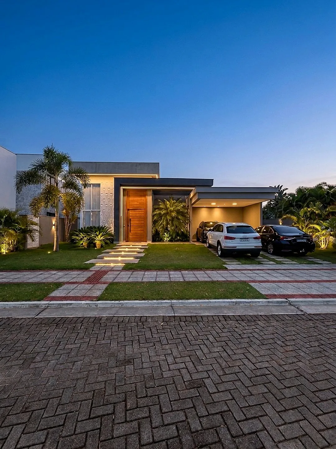 Fachada da casa linear ao anoitecer, com iluminação embutida e garagem coberta